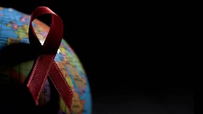 Rote Ansteckschleife auf einem Globus mit viel Schatten vor schwarzem Hintergrund.